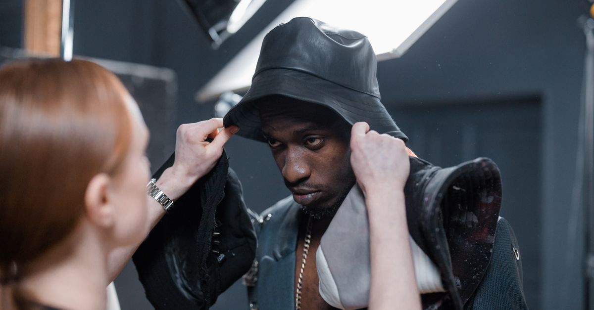 A stylist adjusts a model's outfit during a photoshoot in a studio setting.